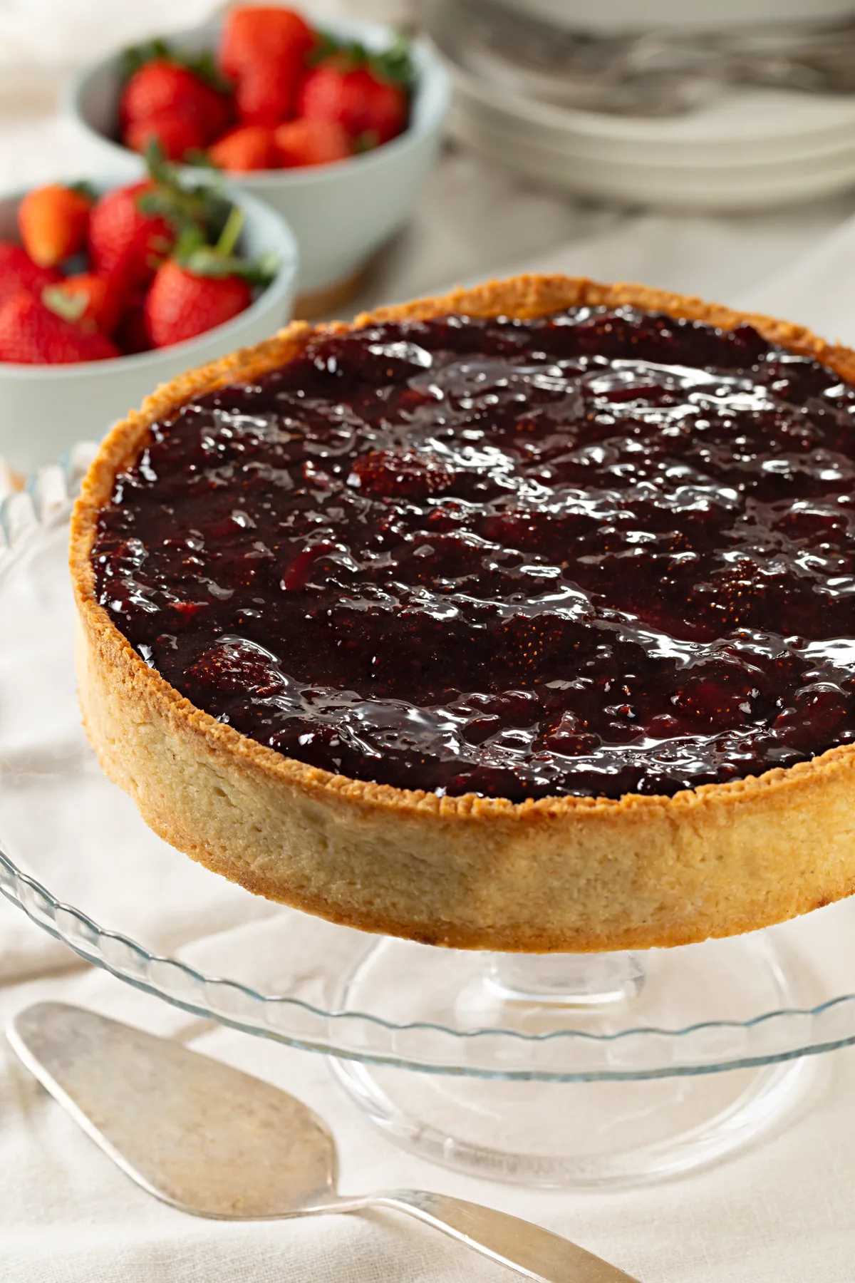 Cheesecake inteira coberta de compota de frutas vermelhas, com morangos ao lado