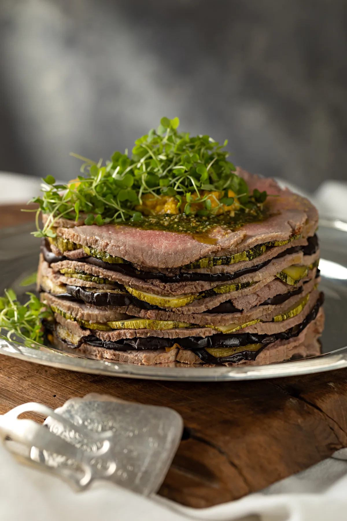 Torre de camadas de roast beef intercaladas com legumes tostados, finalizada com brotos verdes
