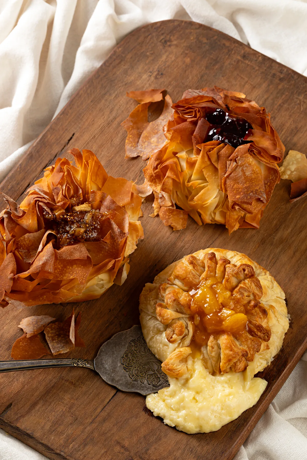 Dois mini bries em massa phyllo sobre tábua de madeira, um deles aberto